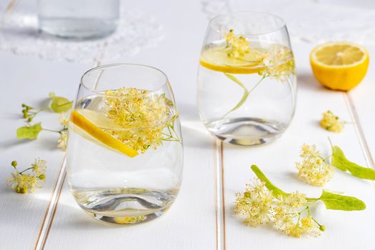 Two glasses of lemonade with fresh linden flowers and lemon
