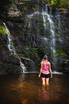 A female stands in the cooling waters of the rock pool after descending off the top of the mountain deep into the ravine  wilderness where this waterfall is located.