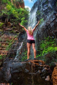 Woman stands on rock in front of cascading waterfall in beautiful Blue Mountains Australia