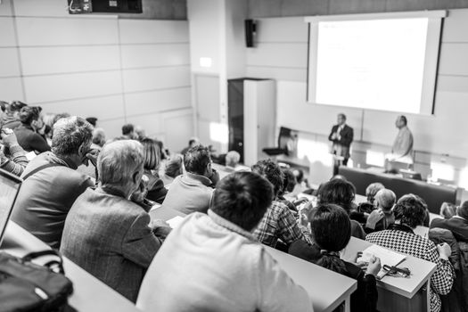 Speaker giving a talk in conference hall at business event. Audience at the conference hall. Business and Entrepreneurship concept. Focus on unrecognizable people in audience. Black and white.