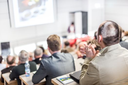 Speaker giving a talk in conference hall at business event. Audience at the conference hall. Business and Entrepreneurship concept. Focus on unrecognizable people in audience.