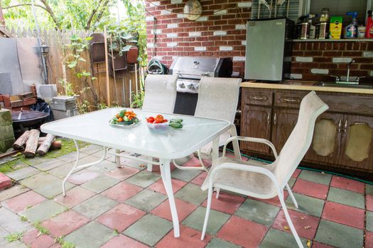 Rustic patio, a table with fresh vegetables and two chairs in the corner of firewood and BBQ