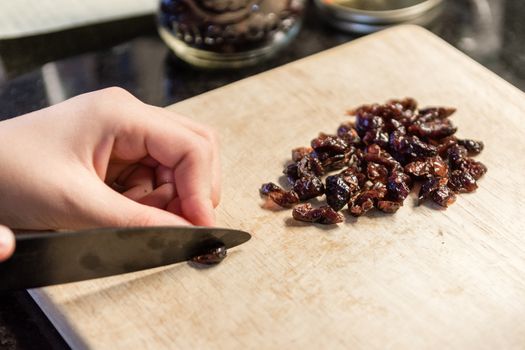 The girl, according to the recipe, slices the raisins into halves for small balls cookies