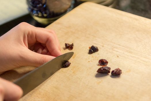 The girl, according to the recipe, slices the raisins into halves for small balls cookies