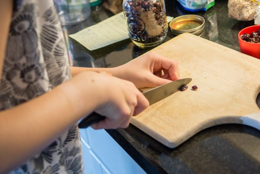 The girl, according to the recipe, slices the raisins into halves for small balls cookies