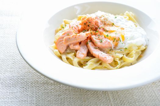 Fettucine with salmon, egg and parmesan cheese, served on white plate.
