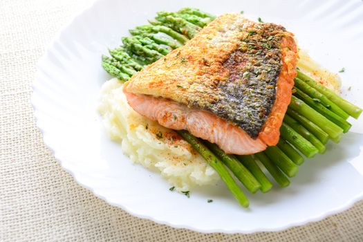 Grilled salmon garnished with asparagus and herbs and mashed potatoes, served on white plated.
