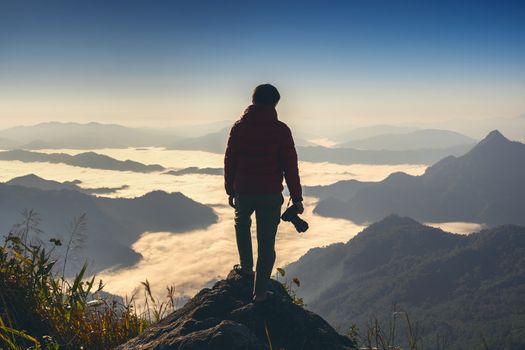 Photographer hand holding camera and standing on top of the rock in nature. Travel concept.