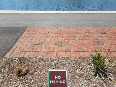 brown no fishing sign with red bricks and river or stream and asphalt