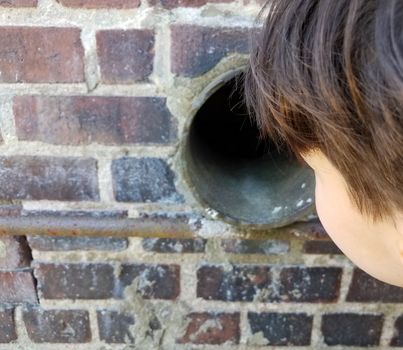 boy child looking though metal pipe or hole with red bricks