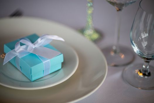 Festive table setting with handmade gift box on plate. Light blue handmade gift box in plate on wedding table.