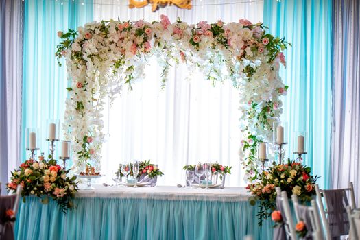 Festive room decorated with flowers. Wedding table setting with bouquets of flowers, candles, glasses and dishes. Decorations and setting for wedding party in restaurant.