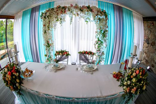 Festive room decorated with flowers. Wedding table setting with bouquets of flowers, candles, glasses and dishes. Decorations and setting for wedding party in restaurant. Shot with fisheye lens. 