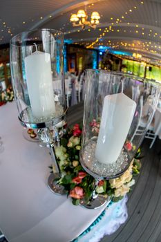 Table decoration for wedding reception. Candlestick with candles and bouquet of flowers on wedding table setting with white tablecloth. Shot with fisheye lens. 