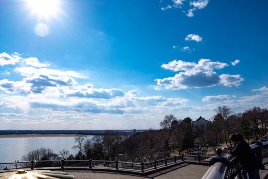 The spring Park is illuminated by the bright sun. View of a large and powerful river. On the bright blue sky beautiful white clouds.