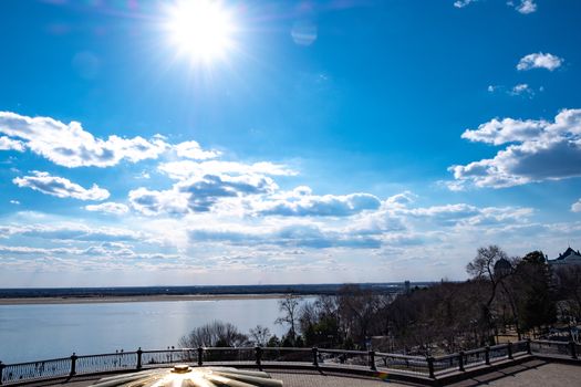 The spring Park is illuminated by the bright sun. View of a large and powerful river. On the bright blue sky beautiful white clouds.