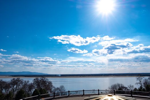 The spring Park is illuminated by the bright sun. View of a large and powerful river. On the bright blue sky beautiful white clouds.