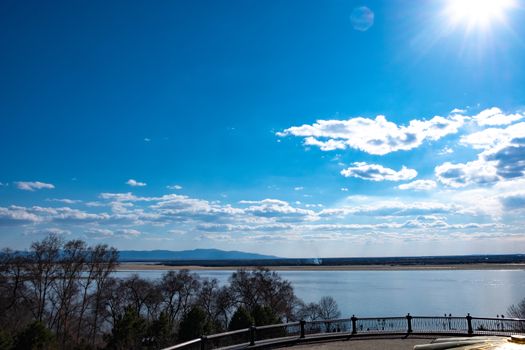 The spring Park is illuminated by the bright sun. View of a large and powerful river. On the bright blue sky beautiful white clouds.