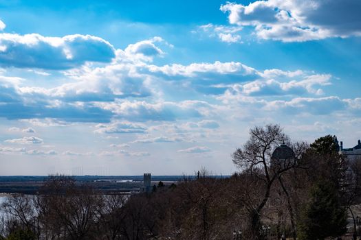 The spring Park is illuminated by the bright sun. View of a large and powerful river. On the bright blue sky beautiful white clouds.