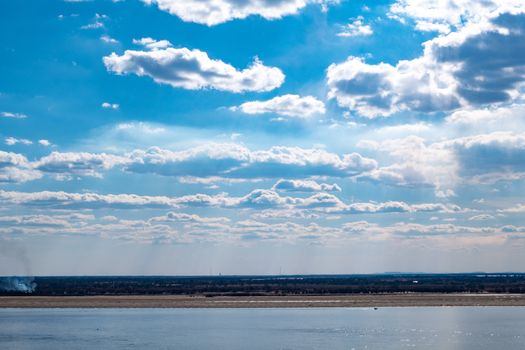 The spring Park is illuminated by the bright sun. View of a large and powerful river. On the bright blue sky beautiful white clouds.