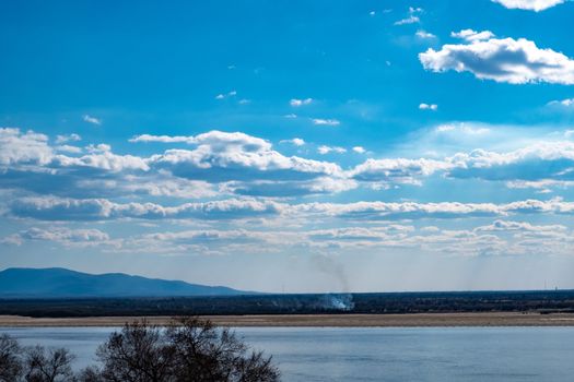 The spring Park is illuminated by the bright sun. View of a large and powerful river. On the bright blue sky beautiful white clouds.