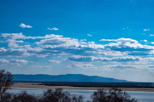 The spring Park is illuminated by the bright sun. View of a large and powerful river. On the bright blue sky beautiful white clouds.