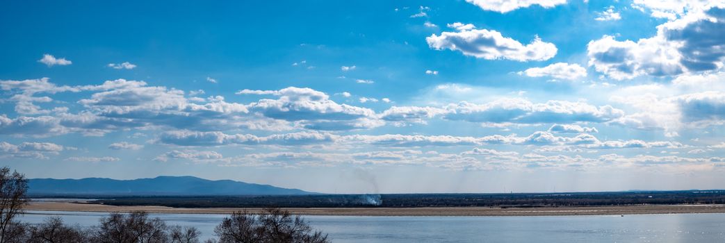 The spring Park is illuminated by the bright sun. View of a large and powerful river. On the bright blue sky beautiful white clouds.