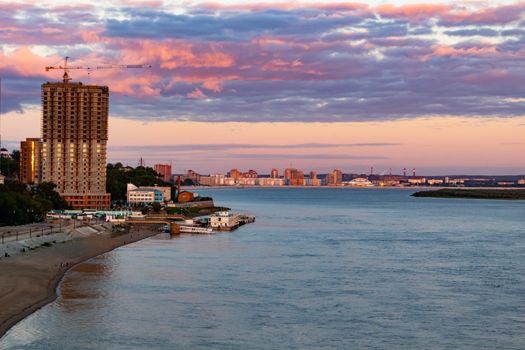 The sun sets over the Amur river. Buildings of the city of Khabarovsk in Golden pink. There are beautiful clouds in the sky.