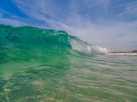 Beach wave curling over with pretty blue sky and wispy white clouds.  Beautiful hot summer day at the beach in Australia