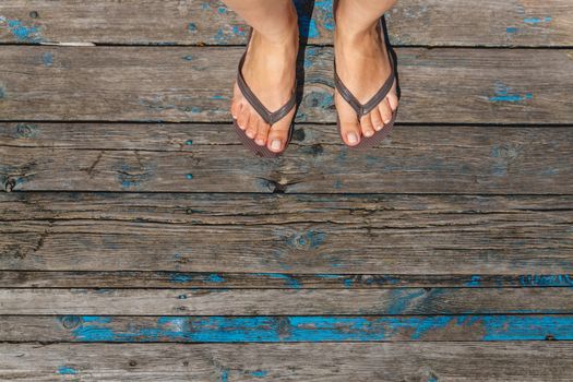 Top view, photo of female legs in beach flip flops on a wooden old floor. Photos on vacation, beach, summer.