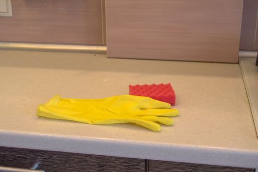 Cleaning tools in the kitchen rubber gloves and sponge lie on the dirty surface of the table, the concept of cleanliness copy space, light from led lamp.