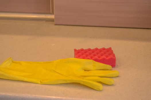 Cleaning tools in the kitchen rubber gloves and sponge lie on the dirty surface of the table, the concept of cleanliness copy space, light from led lamp.