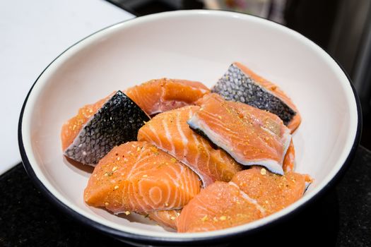 Prepared pieces of trout fillet lie in a white bowl on the kitchen table