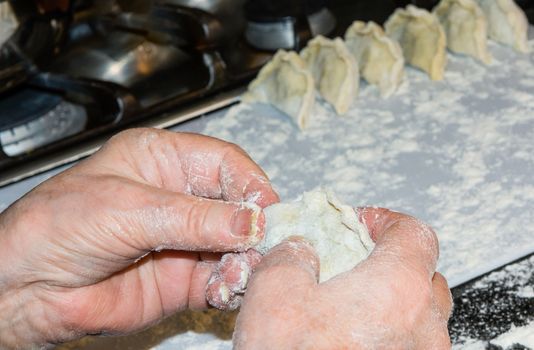 Grandma sculpts dumplings with potatoes and mushrooms and puts them in a row