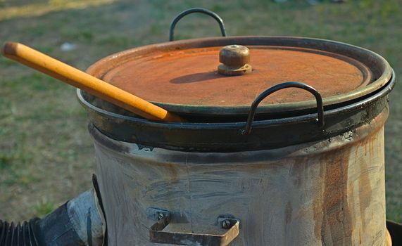 Stove made out of barrel and large covered pot with wooden spoon peaking from it