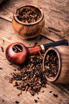 Smoking pipe with tobacco leaves on wooden background