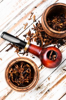 Smoking pipe with tobacco leaves on wooden background