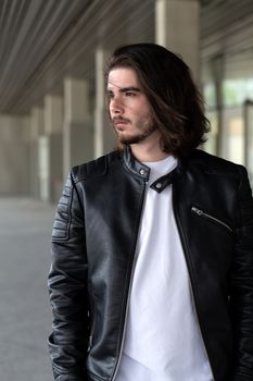 Half length portrait of handsome bearded man dressed in fashionable clothes standing on street against while wall background with area for advertising content. Handsome hipster guy posing on copy space