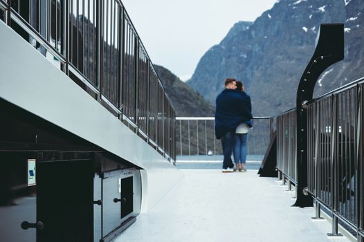 A couple of tourists travels on board a ferry boat. Norway, fjords, mountains in the background. Travel and love concept