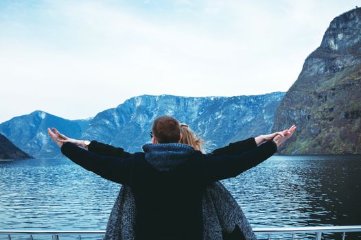 Couple travels by sea ferry in Norway. Fjords and mountains. A couple is standing backs and holding hands. Hands in different directions.
