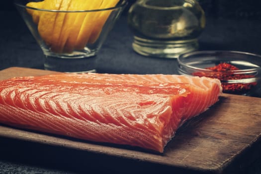 Piece of salmon fillet on a wooden cutting board with ingredients for its further preparation - photo, image.