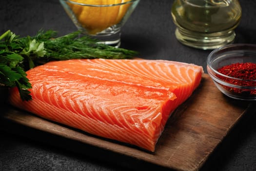 Piece of salmon fillet on a wooden cutting board with ingredients for its further preparation - photo, image.