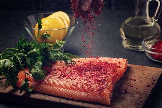 Female hand sprinkles a piece of salmon fillet lying on a wooden cutting board with spices - photo, image,