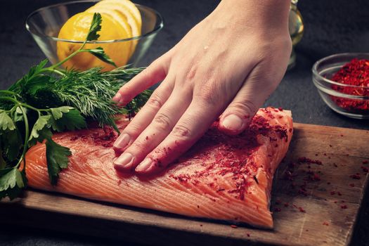 Female hand smears a piece of salmon fillet lying on a wooden cutting board with spices - photo, image,