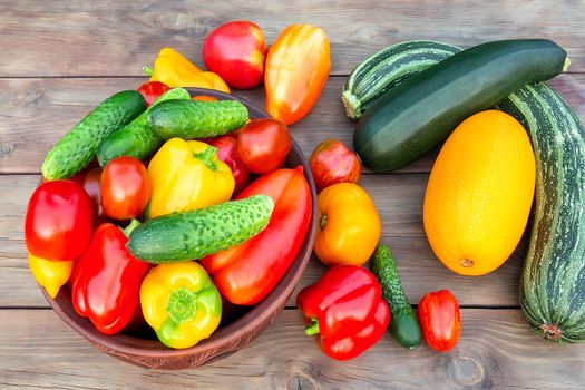 Vegetables: tomatoes, cucumbers, paprika, pepper, zucchini in a clay bowl and on a wooden table. Ingredients for the preparation of summer vegetable salad