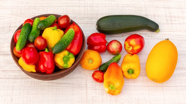 Vegetables: tomatoes, cucumbers, paprika, pepper, zucchini in a clay bowl and on a white wooden table. Ingredients for the preparation of summer vegetable salad