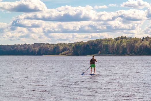 Man standup paddle boarding. Image of young man SUP surfing on the lake.