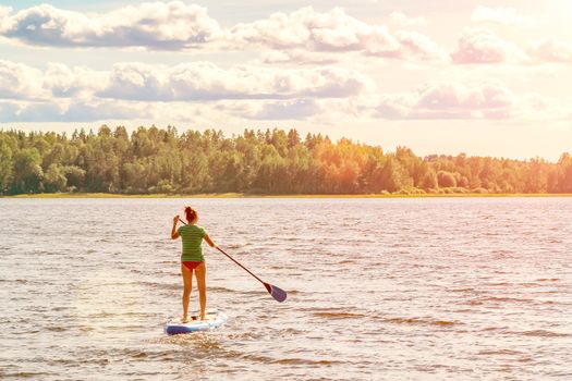 Girl standup paddle boarding. Image of young woman SUP surfing on the lake.