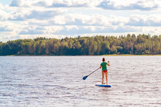 Girl standup paddle boarding. Image of young woman SUP surfing on the lake.