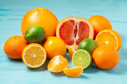 group of whole and sliced citrus fruits - tangerines, lemons, limes, oranges, grapefruits on the surface of the blue table - image.